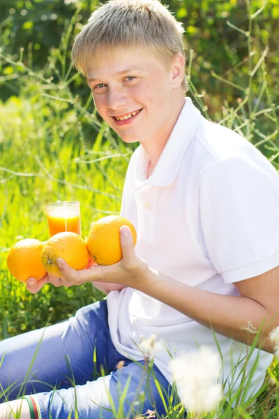 Adolescente chico está sosteniendo vaso con jugo de naranja y frutas — Foto de Stock