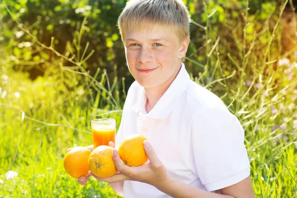 Young boy is holding glass with orange juice and fruits — Zdjęcie stockowe