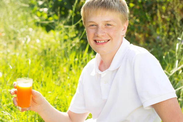 Joven niño está sosteniendo vaso con jugo de zanahoria — Foto de Stock