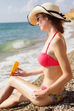 Pretty woman applying sunscreen lotion on her legs
