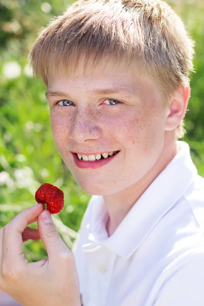 El chico sonriente se pone fresa en la boca. — Foto de Stock