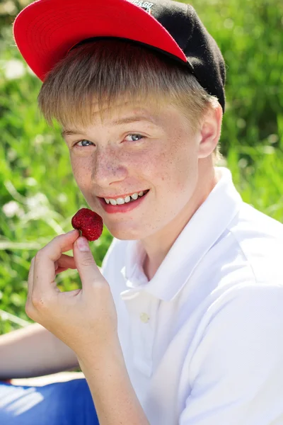 Adolescente chico está usando rojo tapa comer fresa — Foto de Stock