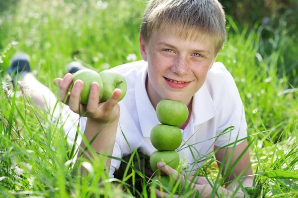 Adolescente chico con pirámide de manzanas verdes acostado en la hierba — Foto de Stock