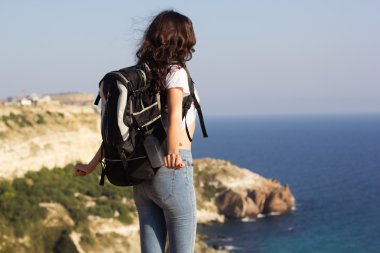 Back view of traveler is standing on rock with backpack