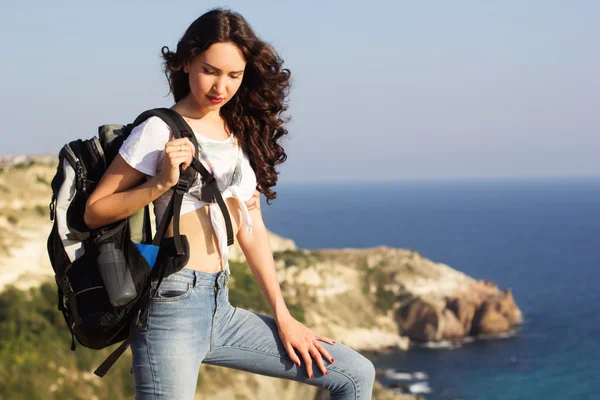 Girl traveler is standing on rock with backpack — Zdjęcie stockowe