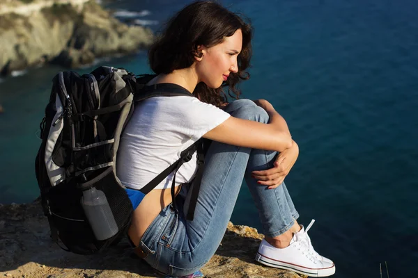 Pretty girl is sitting on rock with backpack — Stock Photo, Image