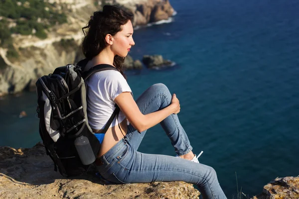 Chica bonita viajero está sentado en el borde de roca con la mochila — Foto de Stock