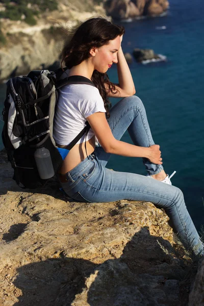 Pretty girl traveler is sitting on rock edge with backpack — Stock Photo, Image