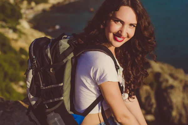 Happy girl with backpack is sitting on rock peak — Stock Photo, Image