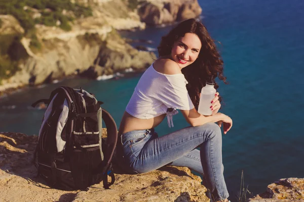 Happy girl backpacker is sitting on rock peak over sea — Stockfoto