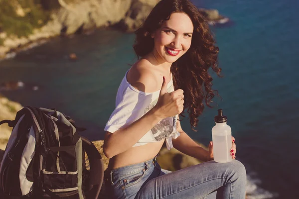 Chica feliz mochilero está sentado en la roca sobre vista al mar — Foto de Stock