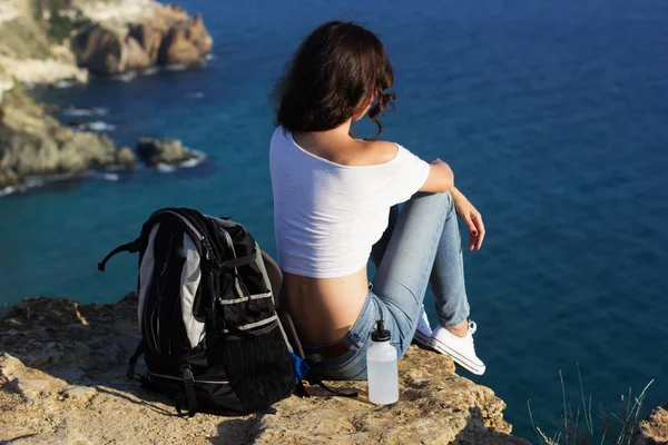 Happy girl backpacker is sitting on rock peak over sea 