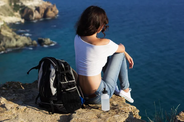 Happy girl backpacker is sitting on rock peak over sea Stockbild
