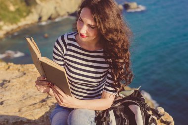 Beautiful woman is reading book on the rock peak 