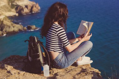 Girl traveler is sitting on mountain peak and reading book