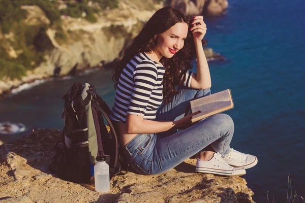 Viajante menina está sentado no pico do rock e livro de leitura — Fotografia de Stock