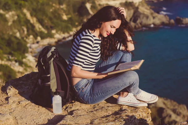 Mulher bonita está sentada no pico do rock e livro de leitura — Fotografia de Stock