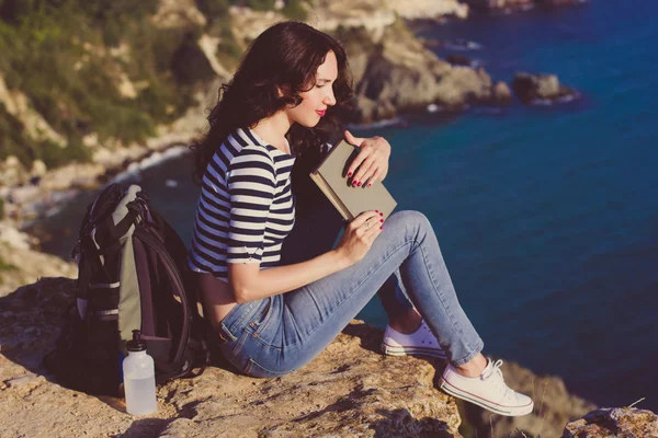 Pretty woman is sitting on rock peak and reading book — Zdjęcie stockowe