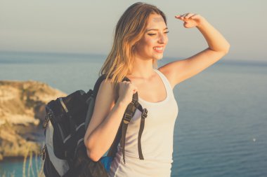 Mutlu backpacker genç kız deniz üzerine kayanın üzerinde duruyor 