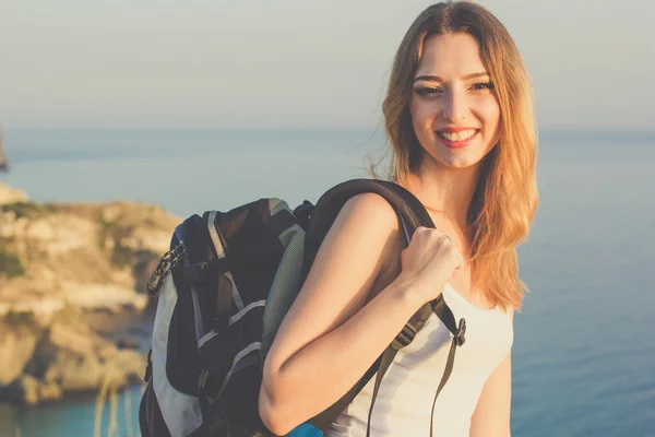 Sorridente zaino in spalla teen ragazza è in piedi su roccia oltre mare — Foto Stock
