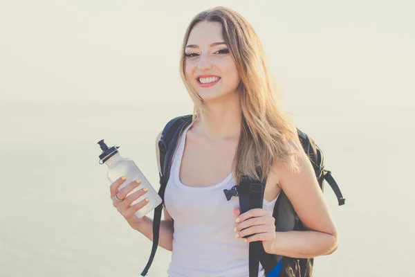 Smiling backpacker girl is holding water bottle