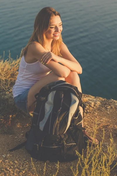 Felice ragazza zaino in spalla è seduto sulla roccia sopra vista sull'oceano — Foto Stock