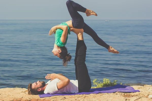 Couple girl and boy are practicing acroyoga on the sea — Stock Photo, Image