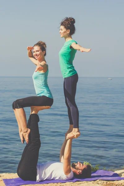 Tres personas deportivas están haciendo acroyoga en la playa — Foto de Stock