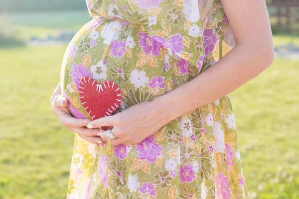 Живот беременной женщины и символ сердца на открытом воздухе — стоковое фото