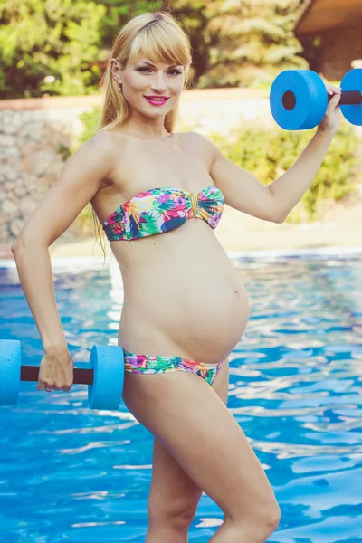 Pregnant girl is doing sport with dumbbells near swimming pool — 图库照片