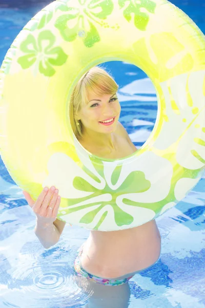 Беременная женщина плавает с зеленым резиновым кольцом в бассейне — стоковое фото