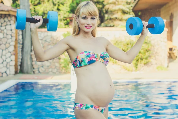 Беременная девушка с гантелями возле бассейна — стоковое фото