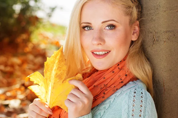 Menina bonita está sentada no parque de outono com folhas de bordo — Fotografia de Stock