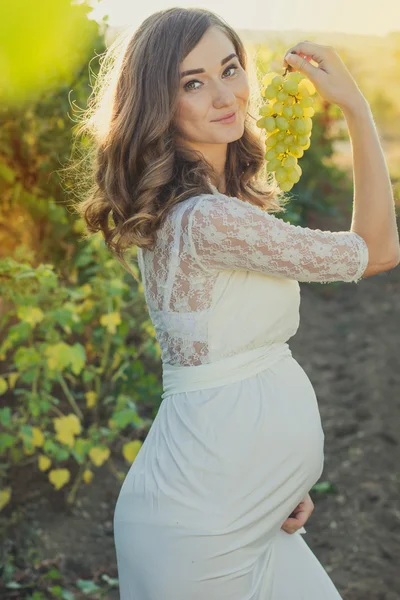 Pregnant girl with bunch of grapes in vineyard — Stock Photo, Image