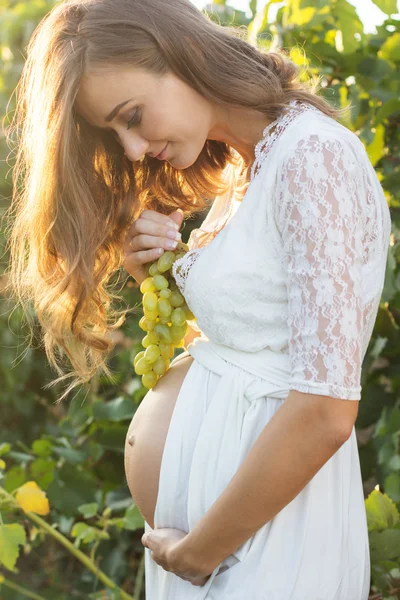 Fille enceinte tenant un bouquet de raisins près du ventre — Photo