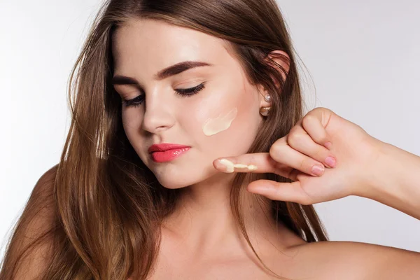 Girl is applying facial cream to cheek — Stockfoto