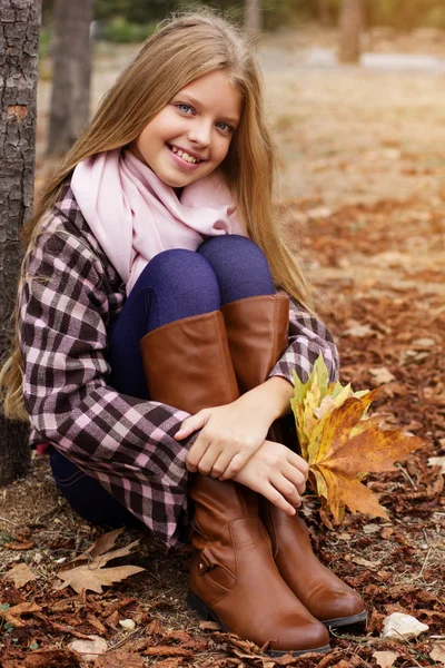 Girl is sitting in autumn park with maple leaves — Stock Photo, Image