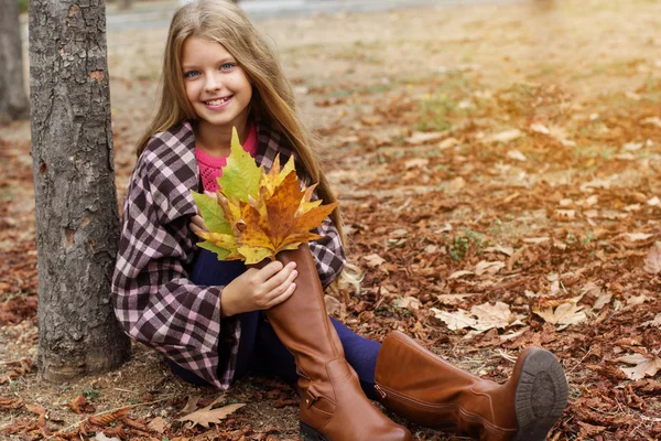 Kız çocuk sarı yapraklar ile parkta oturuyor — Stok fotoğraf