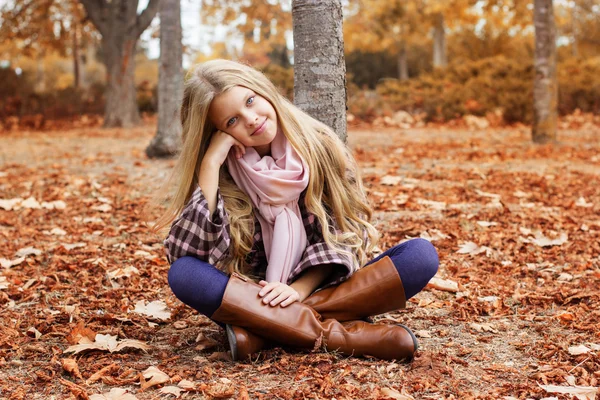 Young girl is sitting on autumn foliage in park — Stock Photo, Image