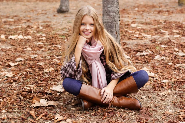 Giovane ragazza è seduta sul fogliame autunno — Foto Stock