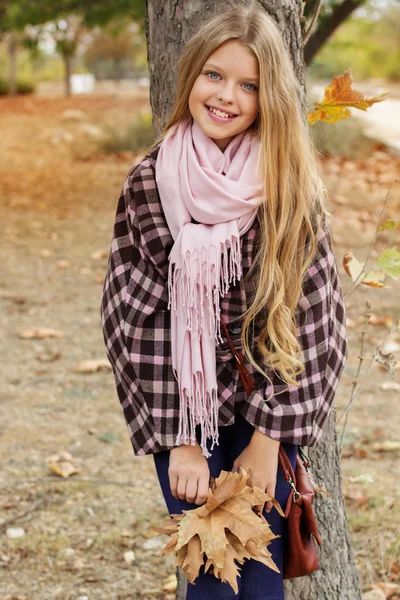 Cute young girl is standing near tree in autumn park — Stock Photo, Image