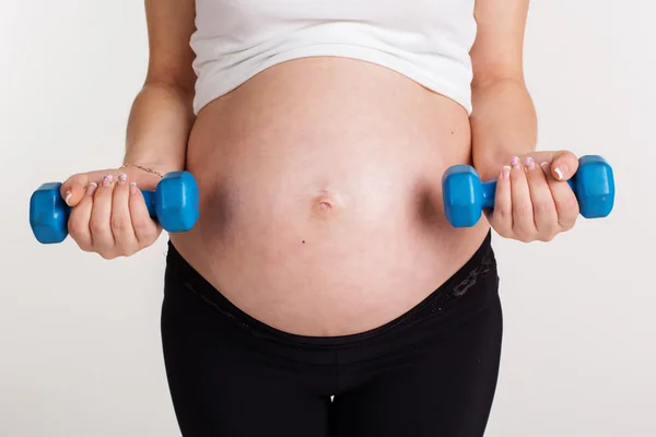 Barriga de mulher grávida com halteres — Fotografia de Stock