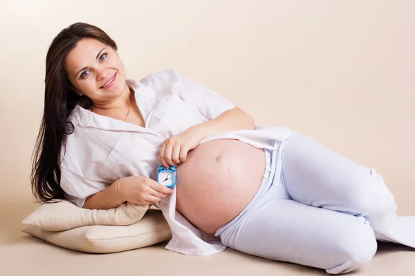 Беременная женщина лежит с подушками и часами — стоковое фото