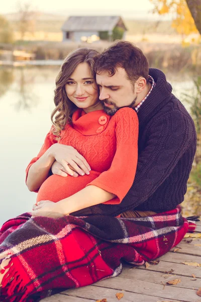 Pregnant girl and man are wrapped in blanket near lake — Stock Photo, Image