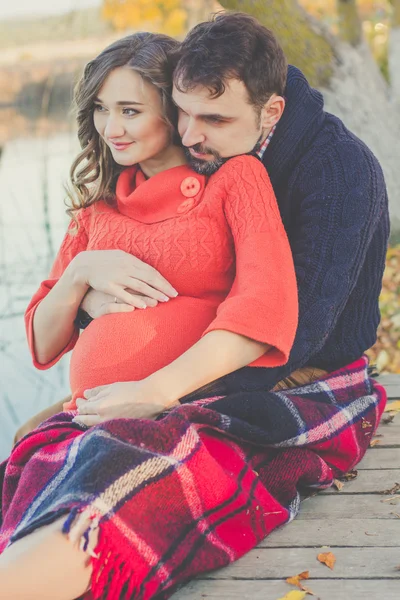 Pregnant woman and man are wrapped in blanket near lake — Stock Photo, Image