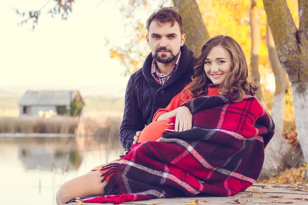 Grávida mulher feliz e homem estão sentados perto do lago — Fotografia de Stock