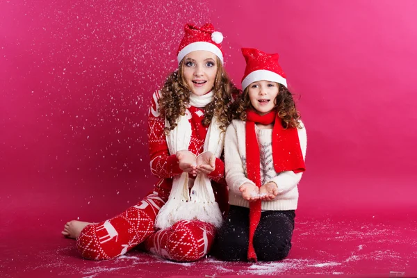 Two cute sisters are blowing fake snow in studio — Stock Photo, Image