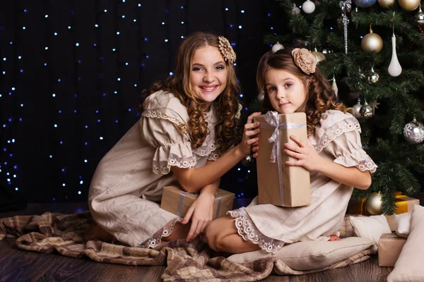 Two girls are sharing gifts near christmas tree — Stock Photo, Image