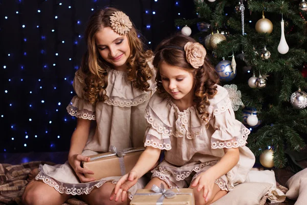 Pretty sisters are sharing gifts near christmas tree — Stock Photo, Image