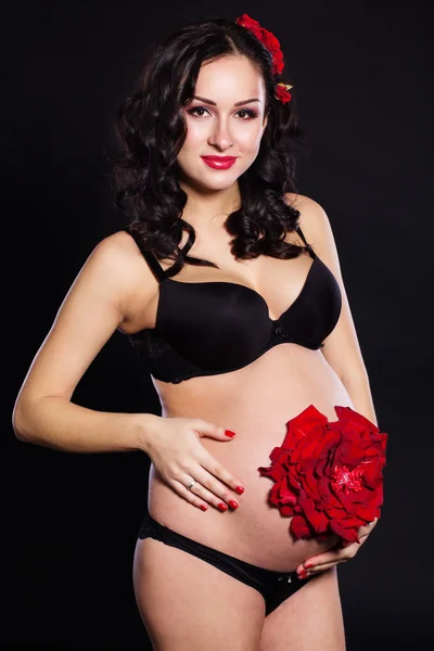 Беременная девочка с красным цветом розы на животе — стоковое фото